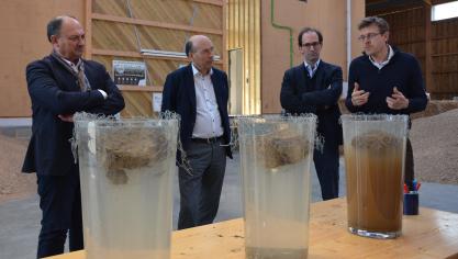 Willy Borsus, Olivier de Wasseige, Chuck de Liedekerke et Nicolas Verschuere (de gauche  à droite) observent les résultats du « slake test »: dans le récipient de droite, la motte  issue d’une parcelle intensive se désagrège rapidement tandis que les mottes  « régénérative » et « forestière » ne se délitent que très peu.